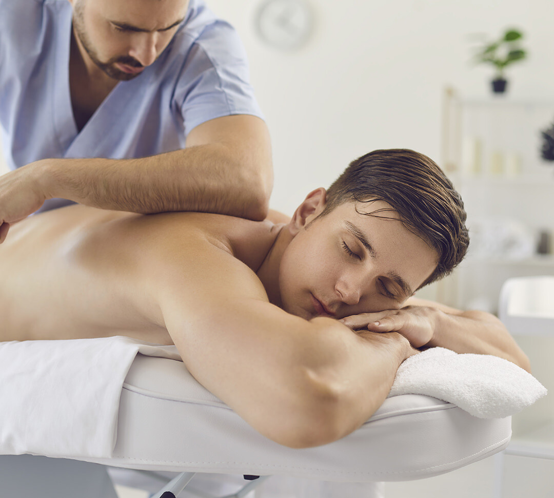 Ein junger Mann liegt entspannt auf einer Massageliege und entspannt eine professionelle Massage von einem Physiotherapeuten
